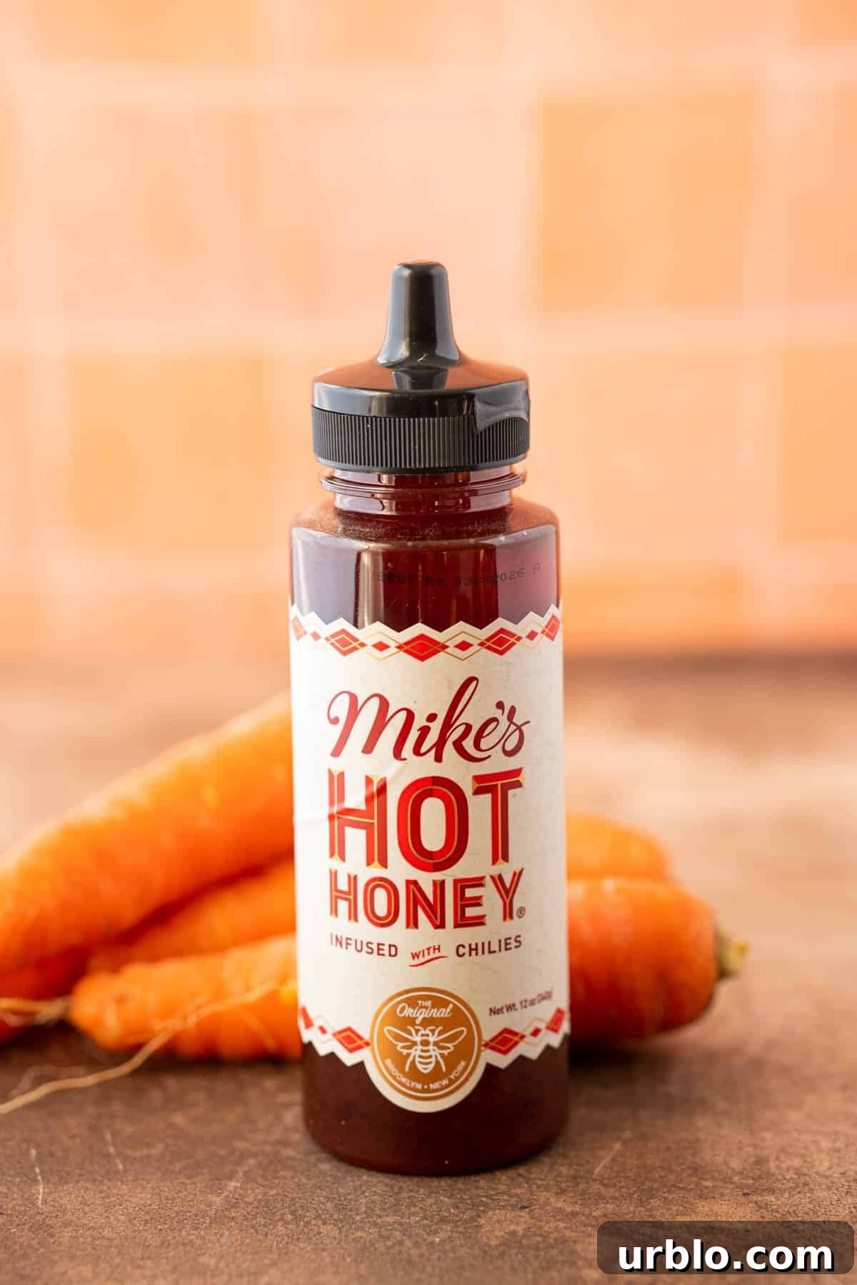 Spicy Honey-Glazed Carrots with Brown Butter and Herbs 3 A bottle of hot honey on a table with carrots behind it.