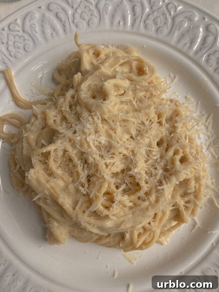Creamy Vegan Cauliflower Spaghetti with Cheese Sauce Made From Cauliflower with Vegan parmesan sprinkled on top on a glass plate. 