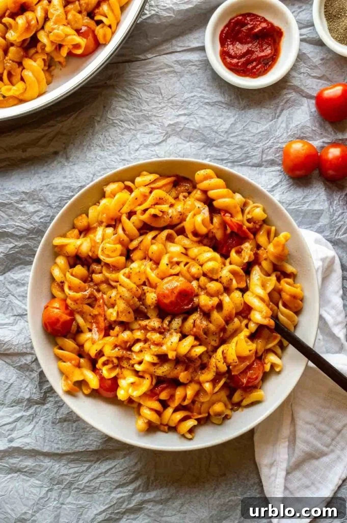 Top down view of a bowl of pasta with cherry tomatoes and an orange sauce, on a pale grey background