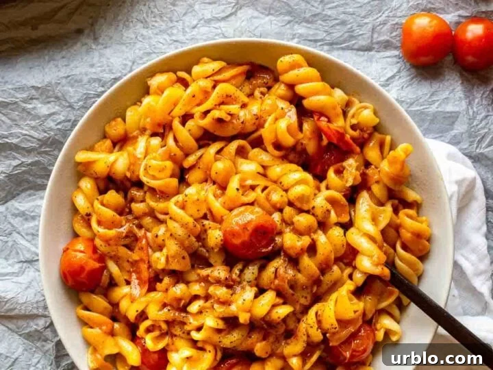 Top down view of a bowl of pasta with cherry tomatoes and an orange sauce, on a pale grey background