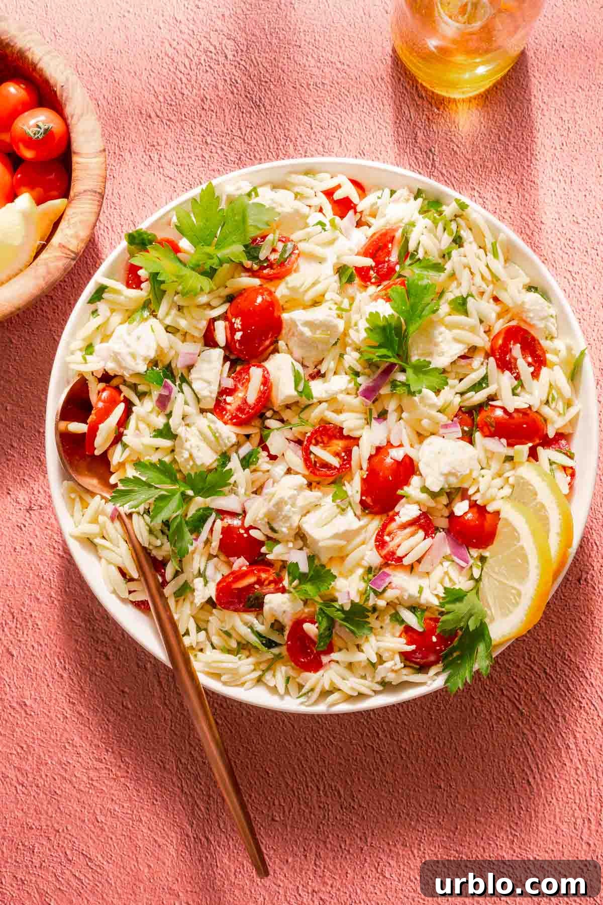 orzo salad with feta lemon and tomatoes in bowl with olive oil bottle on the side.