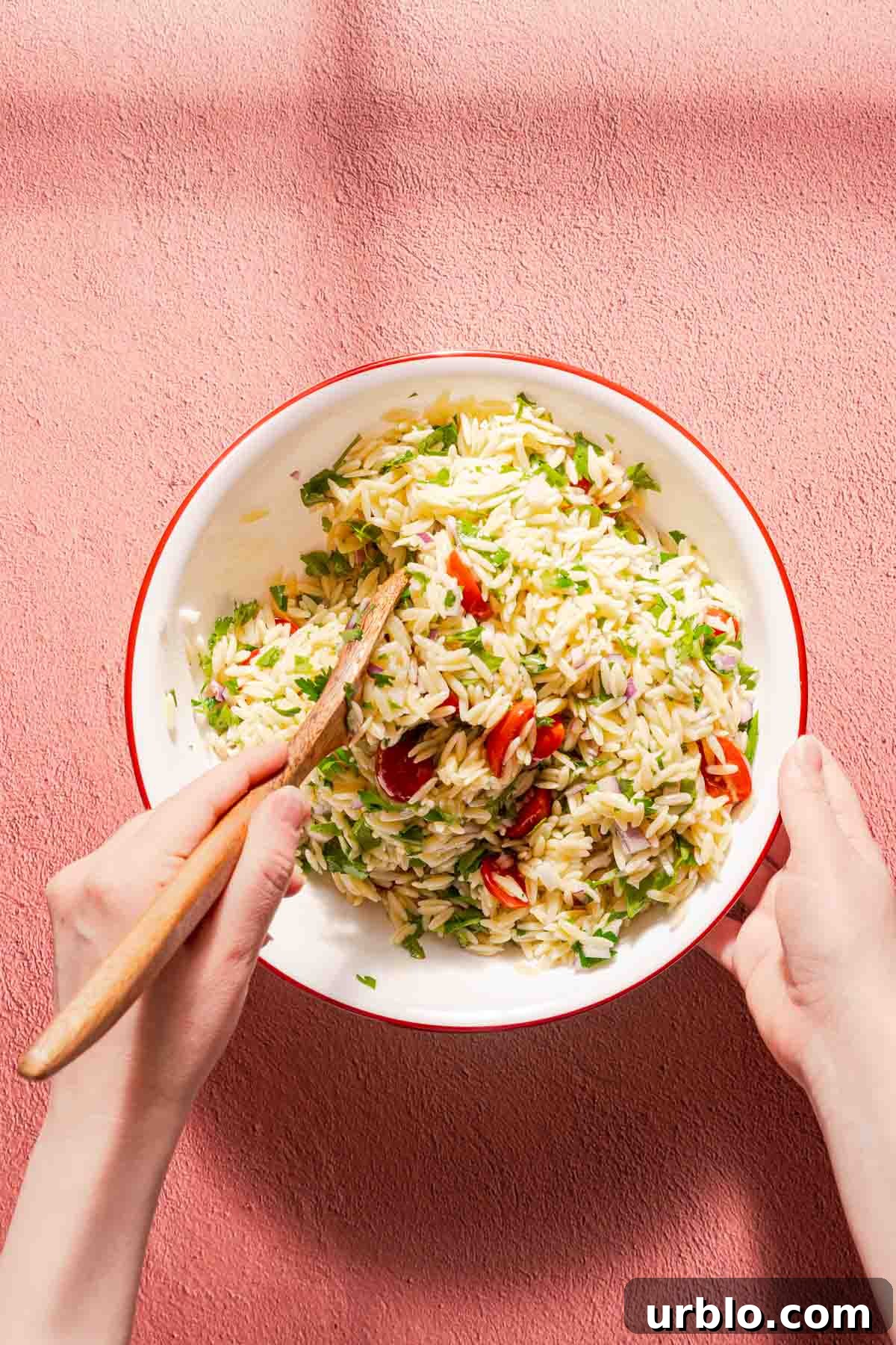 orzo salad being mixed in a large bowl with a wooden spoon.