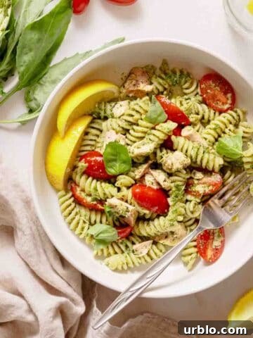 bowl of pesto pasta with tuna and tomatoes with lemon on the side.