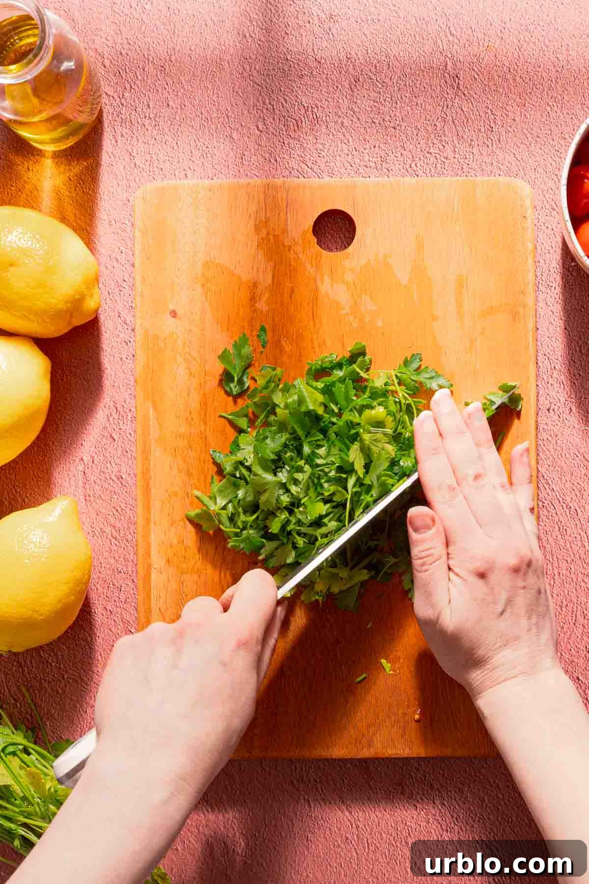 parsley being chopped on wooden cutting board.