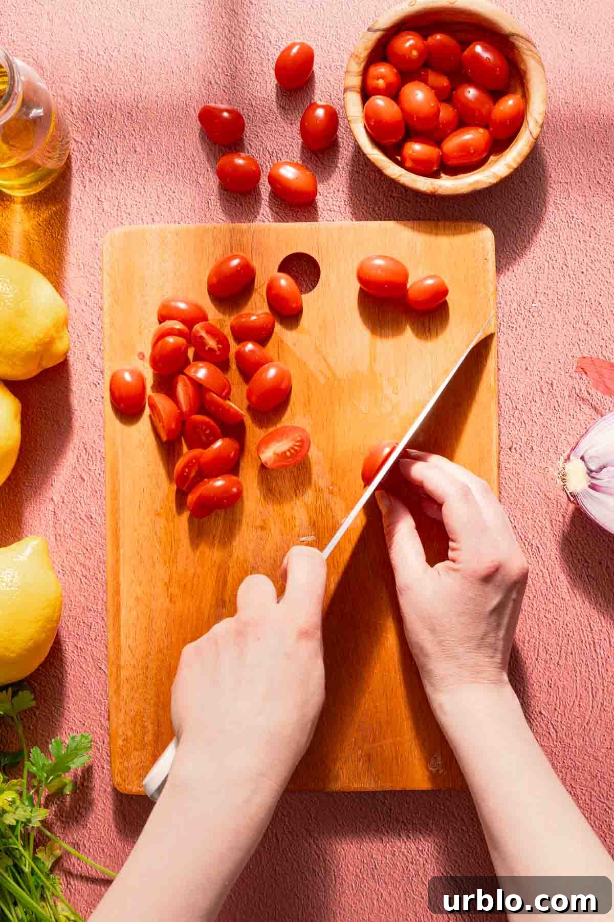 grape tomatoes being cut in half on wooden cutting board.
