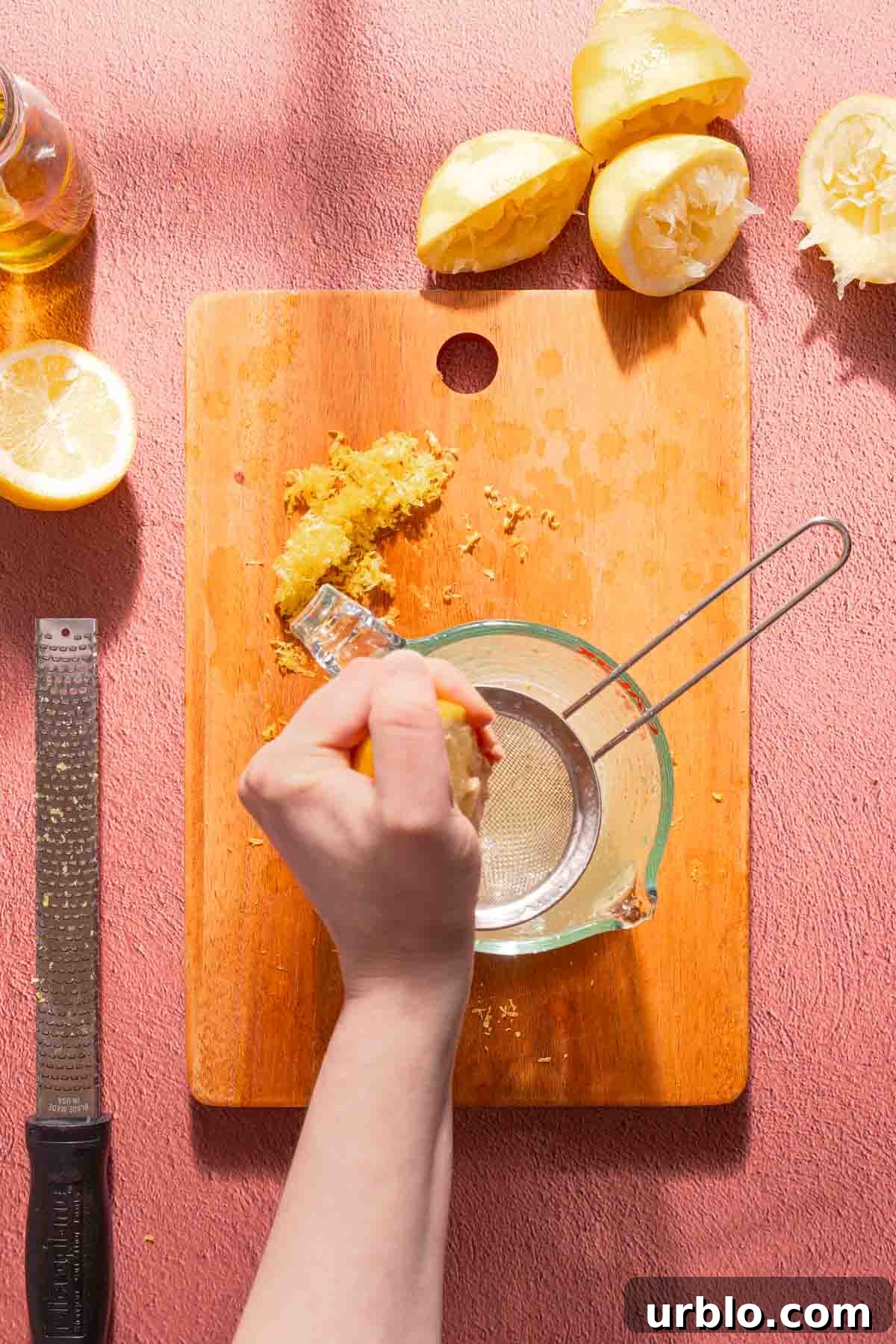 lemon half being squeezed over sieve sitting in measuring cup.
