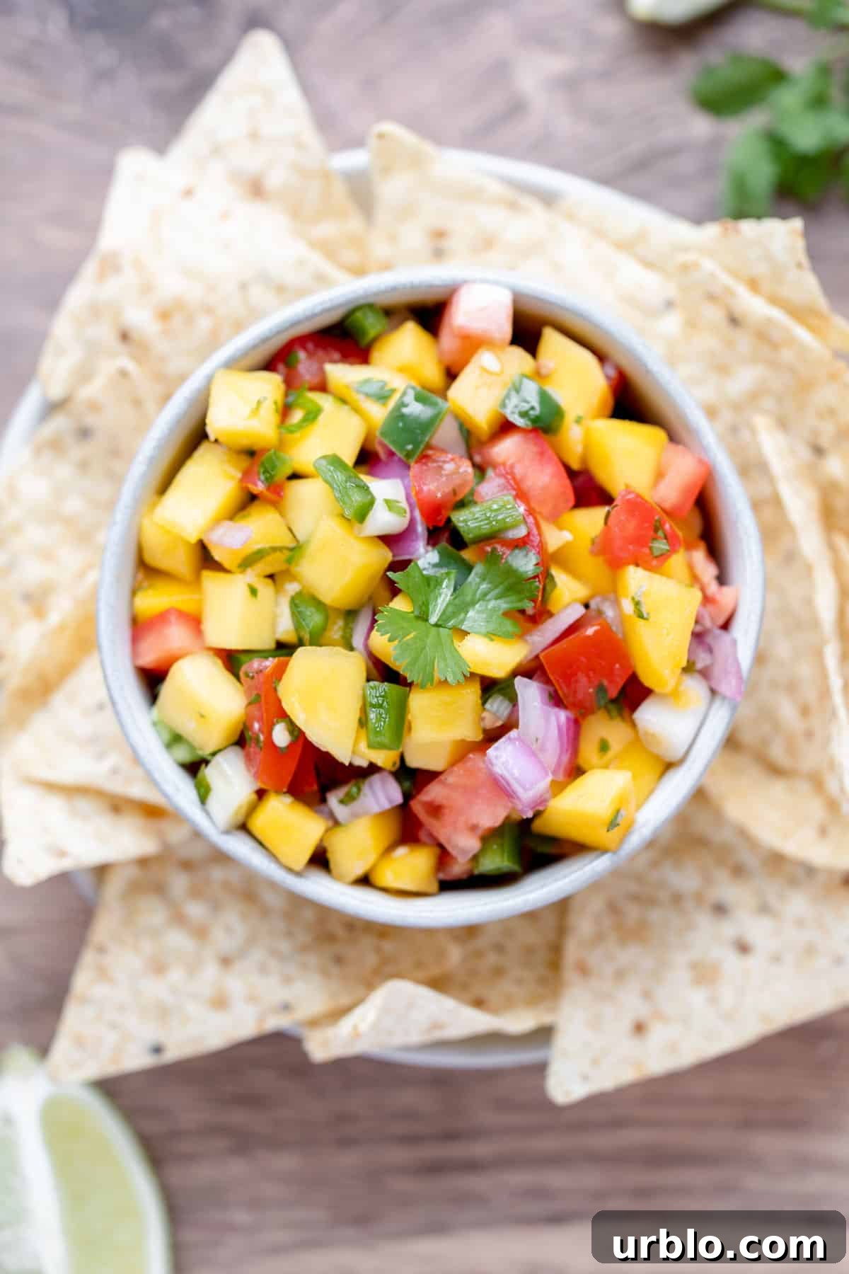 A bowl of mango pico de gallo with chips, lime wedges and fresh cilantro