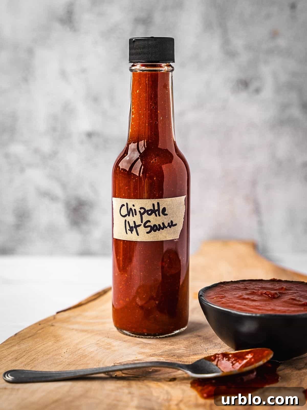 Bottle of hot sauce on a board next to a small bowl with the same hot sauce.