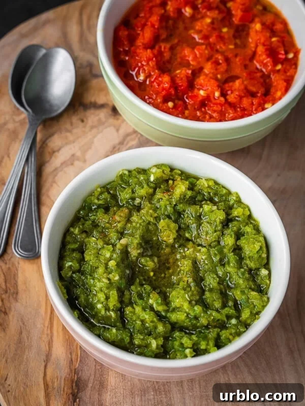 Two bowls of chili paste, one green and one red, on a wooden board.