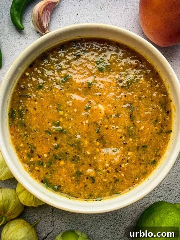Peach tomatillo salsa in a bowl surrounded by ingredients.