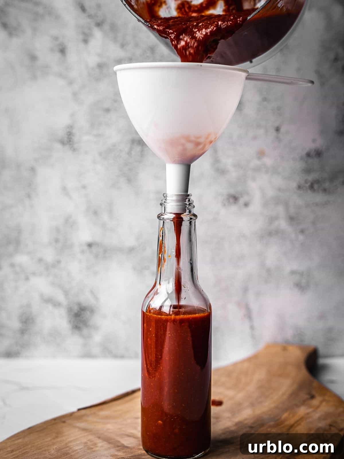 Pouring the finished hot sauce through a funnel and into a glass hot sauce bottle.