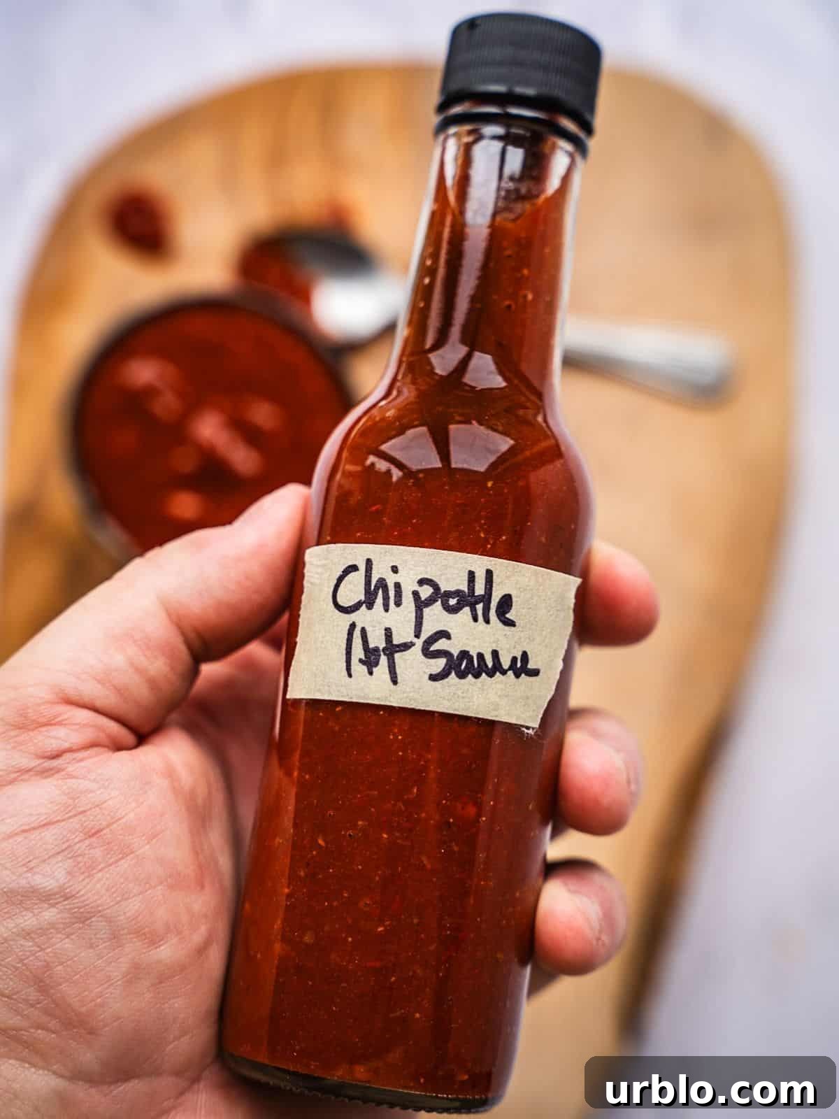 Hand holding a bottle of hot sauce labeled chipotle hot sauce.