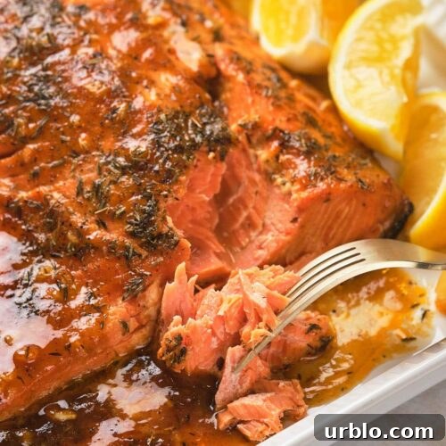 Honey mustard glazed salmon with a herb glaze on a white plate, accompanied by lemon wedges.