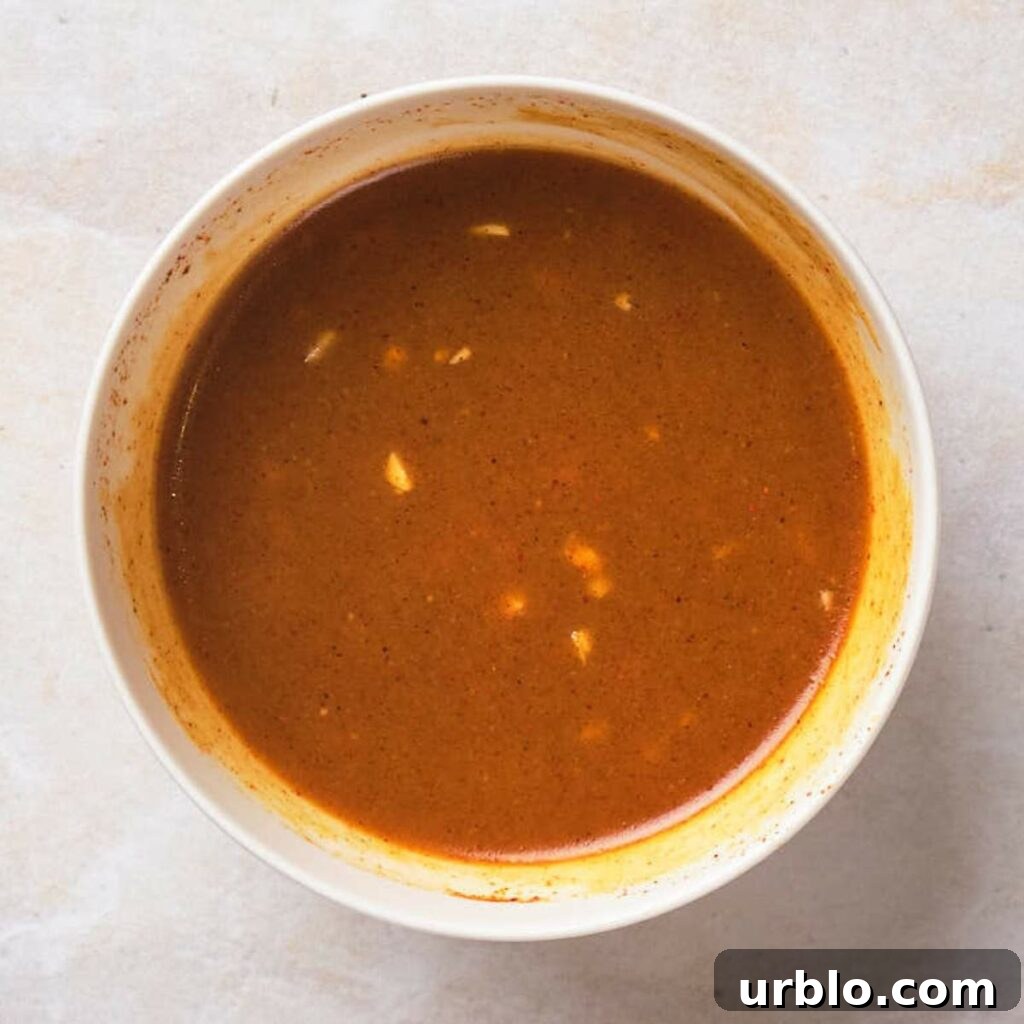 A white bowl filled with brown sauce, showing small bits of spices and garlic.