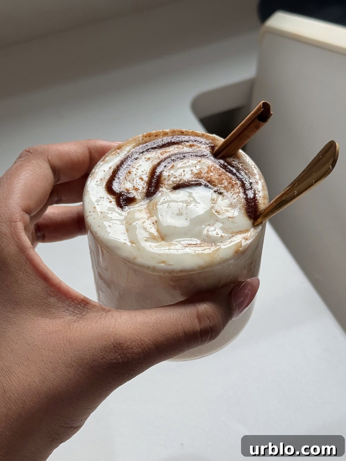 A hand holding a cup of cinnamon roll overnight oats.