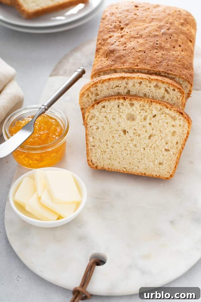 Sliced loaf of English Muffin Bread next to butter and jam on a marble board