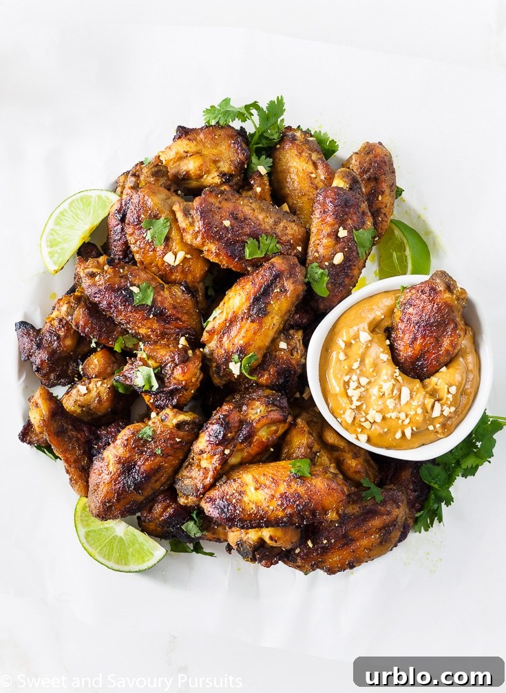 Platter of Thai Chicken Wings with a chicken wing dipped in a bowl of peanut sauce.