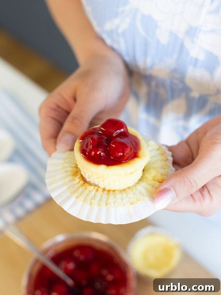 Mini Cherry Cheesecakes Made in a Muffin Tin 9 Close-up of a mini cheesecake topped with cherry pie filling in a white cupcake liner.