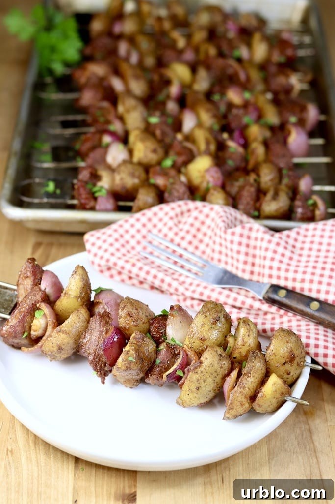 Quick weeknight dinner made with sirloin steak, potatoes and onions plated steak and potato kabob with red napkin, fork and sheet pan of kabobs in background