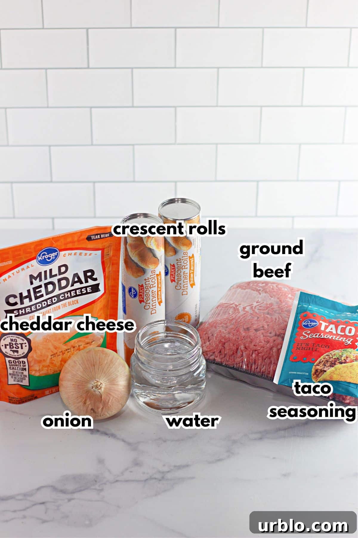 Cheesy Taco Ring with Crescent Roll Crust 4 bag of cheddar cheese, two cans of crescent rolls, onion, water, taco seasoning packet, and a package of ground beef on a counter.
