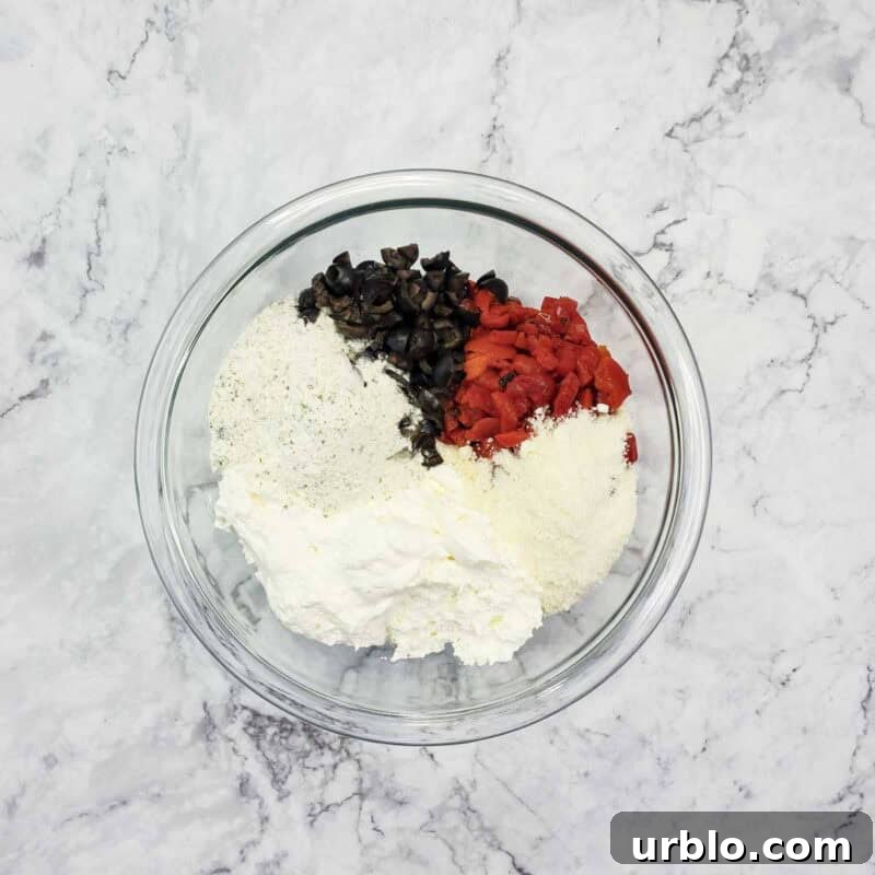 Creamy Ranch Pinwheels with Roasted Red Peppers Appetizer 5 Overhead view of process shot 2 - in a medium bowl, combine the cream cheese, ranch dressing mix, parmesan cheese, chopped red peppers, and chopped olives.